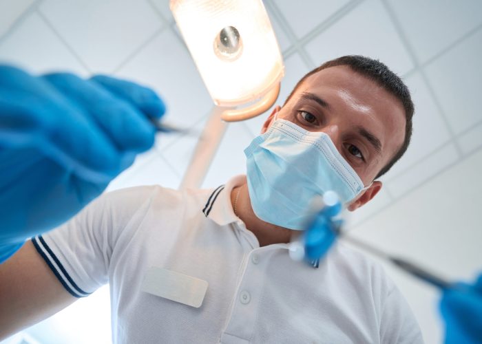 Low angle of professional dentist in disposable nitrile gloves and face mask working with medical instruments