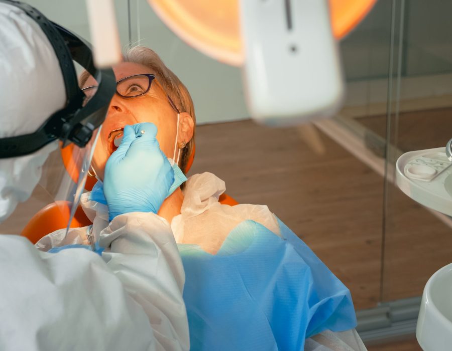 Woman on dental chair in dentist surgery treated with dental drill during covid-19 pandemic. Orthodontist lighting the lamp wearing face shield, protection suit, mask and gloves talking with patient SSUCv3H4sIAAAAAAAACnRSTW/cIBC9V+p/WPkcVGPAhtwr9ZJbb1UPwwC7KKyJbJwoivLfO7bXWw7tBTFvHo83Hx9fv5xOjYU5YvN4+lgjimNKy1wmKDGPBLcPN3zyo/NTjXgXS54ipBq0UPAywtUTOC4prfDnlmzmAmWZ/bx+doMQij+Txg7eJXZHv/b4dCS2JL2gVPPDQyoXhMl/eyIfSCYeKta82JX1FGf0KcHo8zI3R37/+z/CPz3Zzymf3/8l+D15LFMeI1Zy++X30QE4+xHftyKr4iefPOzF3+pqnDIALVimgtJMBjcwHXBggc5eGW7QhMNEw3vey1YJhhIMk33omekxMO2xBS+E6ZS4k93gUAkiB9Uikb1nGgJnrdbWtCidFOpO7p1UAzeadQiCybZrmTaDYyAG3jnbAXd/baggbc+lY0immVRWM9B0eHCt6NEYVHLrzN6O5vmt+OlajxwWF3M17ddMw1sJourWyxQxjufqWS6XbfuOZ5iXsUxrm5u7uZTzC9i0rl4gTX/gF5hnorsDrz5C2vV8rf4Zc9mGdFNtHG3oGnLRSa14ryTv6NYJfiPsW32JpLPZOYQoxufo6tLj6qAJQQlQBplSmsbO0TBrTcf6oW+d9UNnuaIWfv4BAAD//wMA7gjRoZ8DAAA=