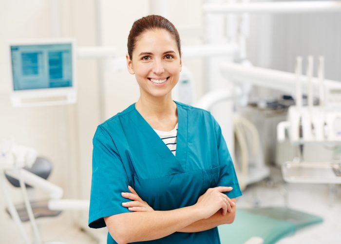 Happy young dentist or surgeon in uniform with crossed arms on her chest